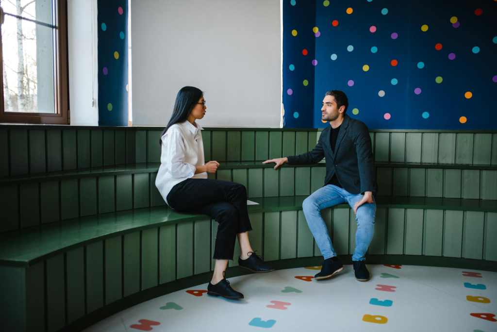 two teachers sit having a conversation inside a classroom