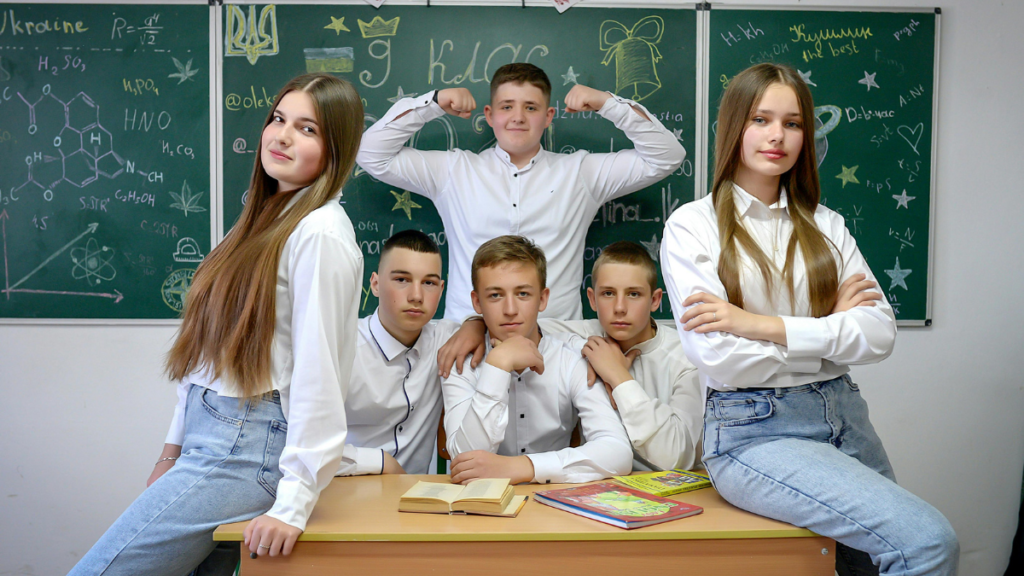Students gather around a desk with confident and strong postures indicating a classroom behavior system that is effective and well-liked.