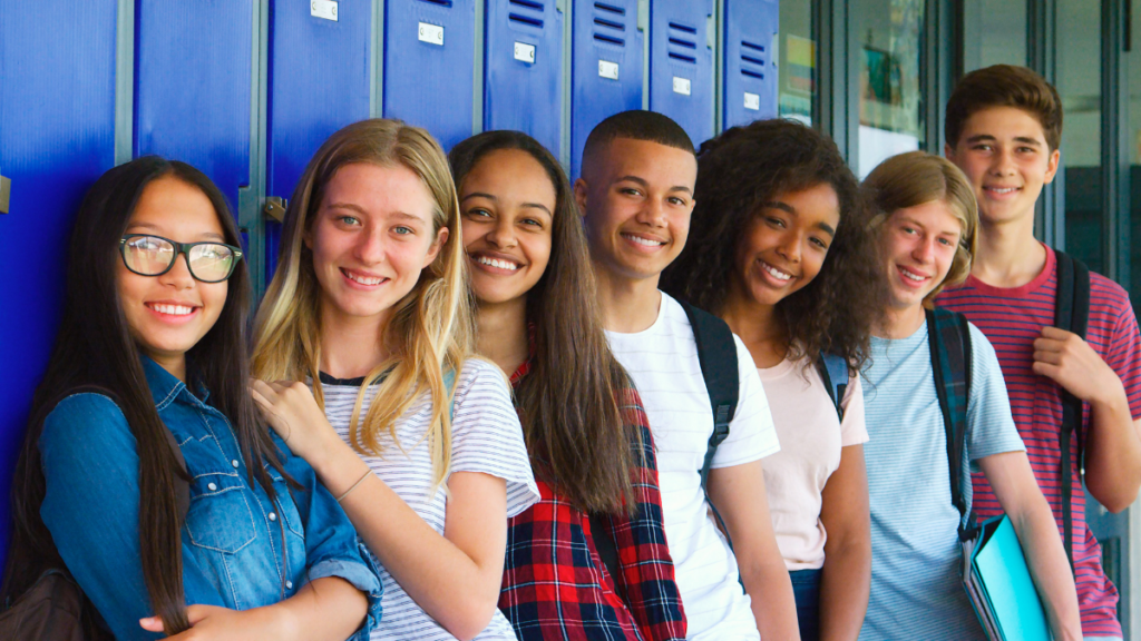 Older students in grades 4-8 stand in an orderly row in front of a bank of lockers. The students are smiling and are not rowdy, showing an effective classroom transition strategy.