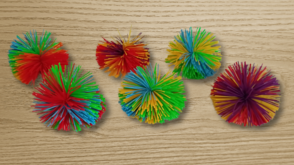Six stringy balls (sometimes called Koosh balls) sit on a wooden desk top.