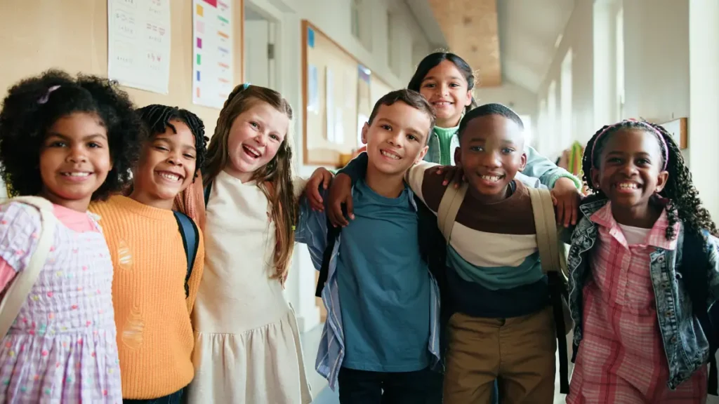 Eight upper elementary students of mixed races stand in a hallway together and smile, showing responsibility and self-regulation in the classroom
