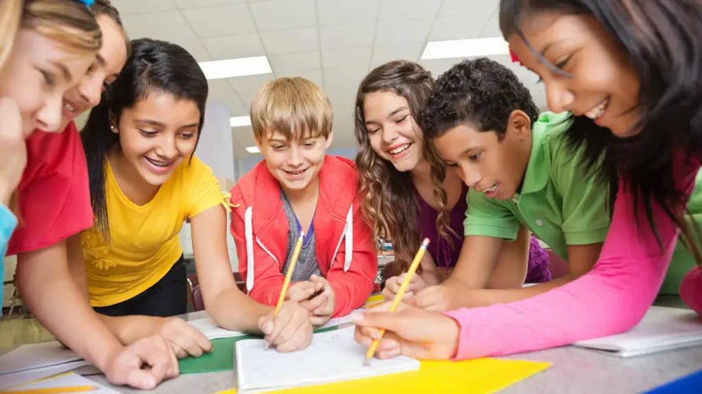 Students in older grades lean over a notebook and work and write cooperatively, showing an effective learning environment with strong classroom management