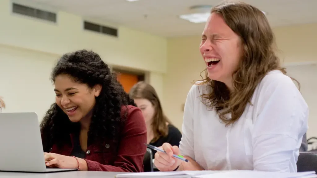 Two older middle school students attempt to work on a computer project while laughing and distracting each other, indicating a possible need for a brain break