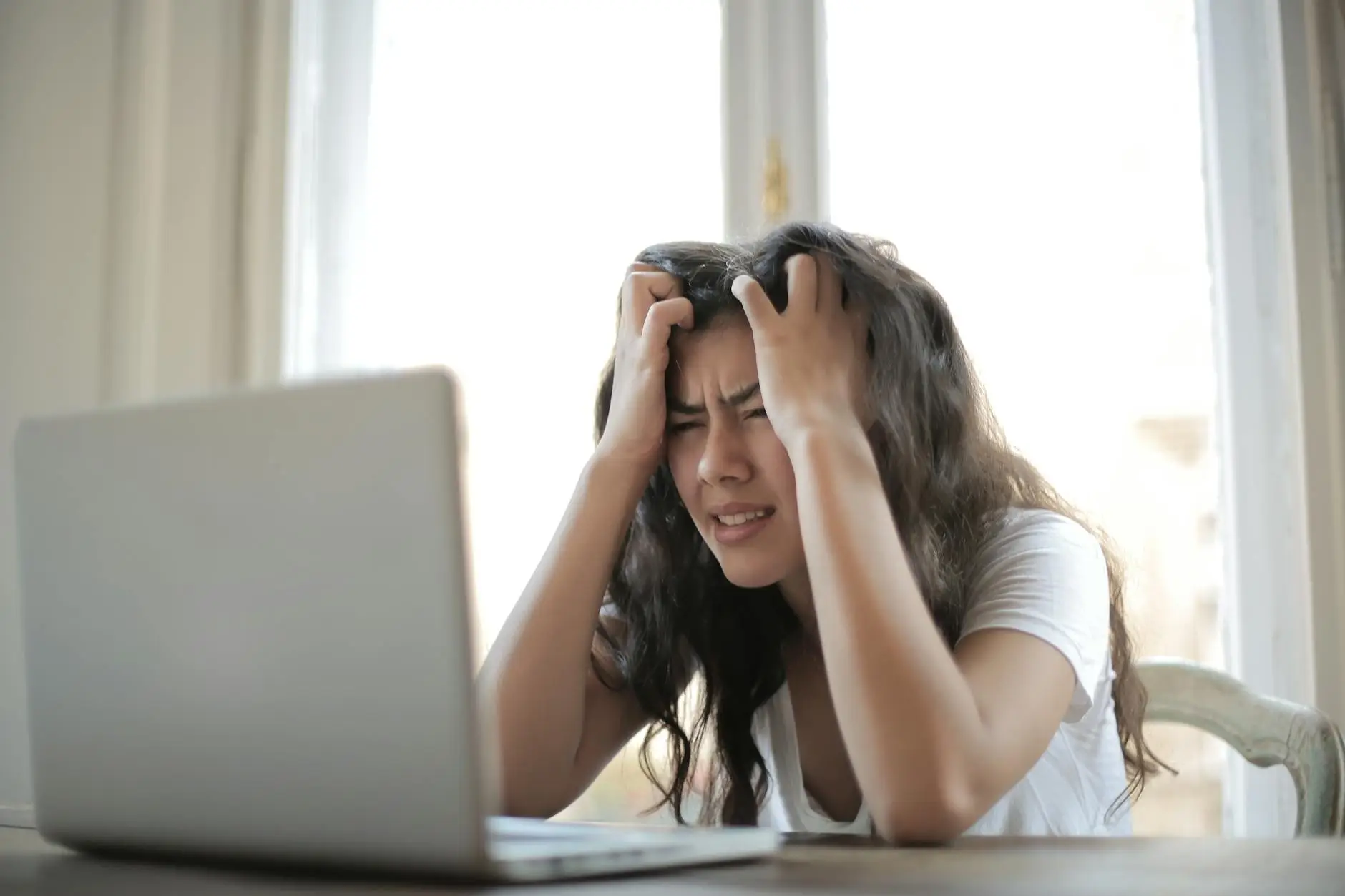 A student sits in front of a computer and digs her fingers into her hair. Her face is scrunched up and she is squinting at the screen, showing frustration or an inability to complete the task on her own.