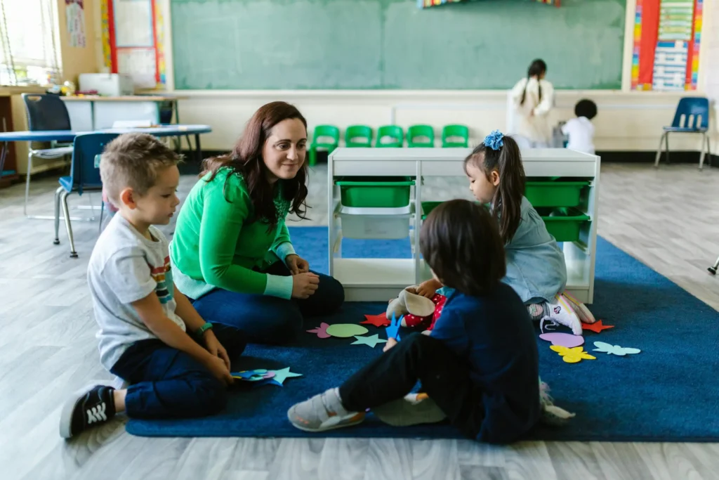 Teacher and children engaged in a class meeting on a carpet on the floor.