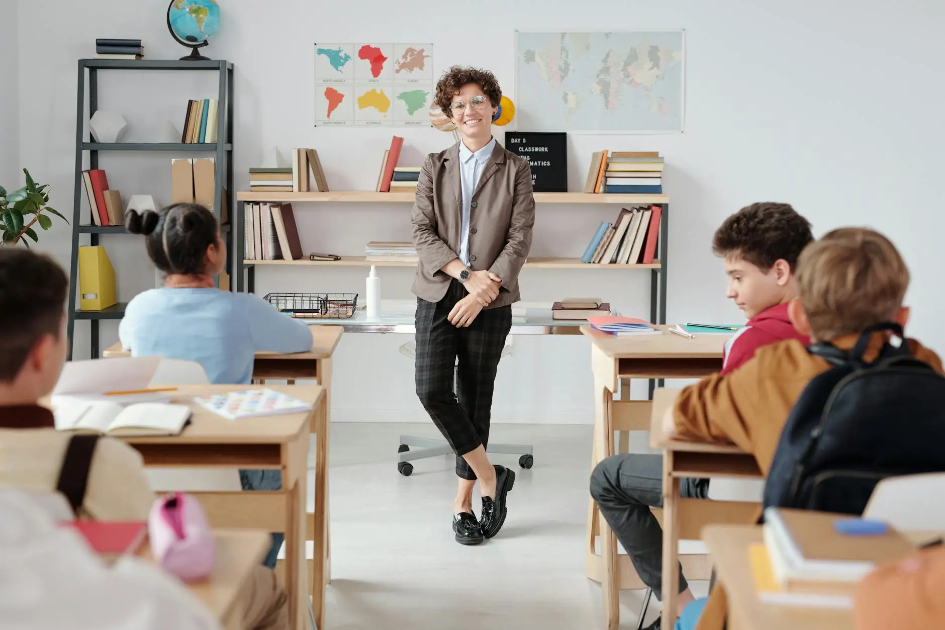 A teacher stands at the front of her classroom and smiles confidently. Students sit in neat rows before her, ready to start the school year on the right foot.