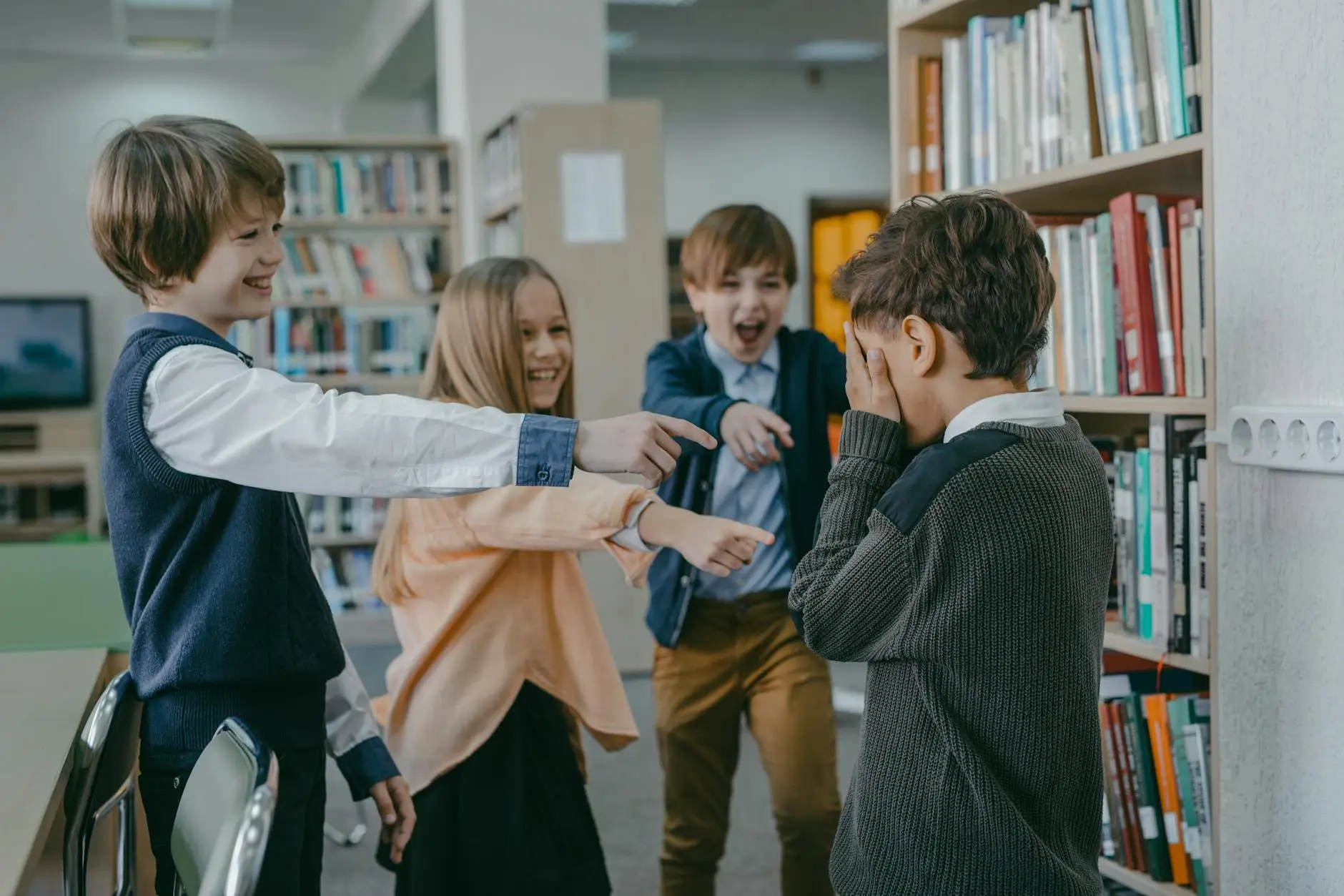 A group of upper elementary students point and laugh at a boy who buries his face in his hands, showing a need to revisit the classroom management plan