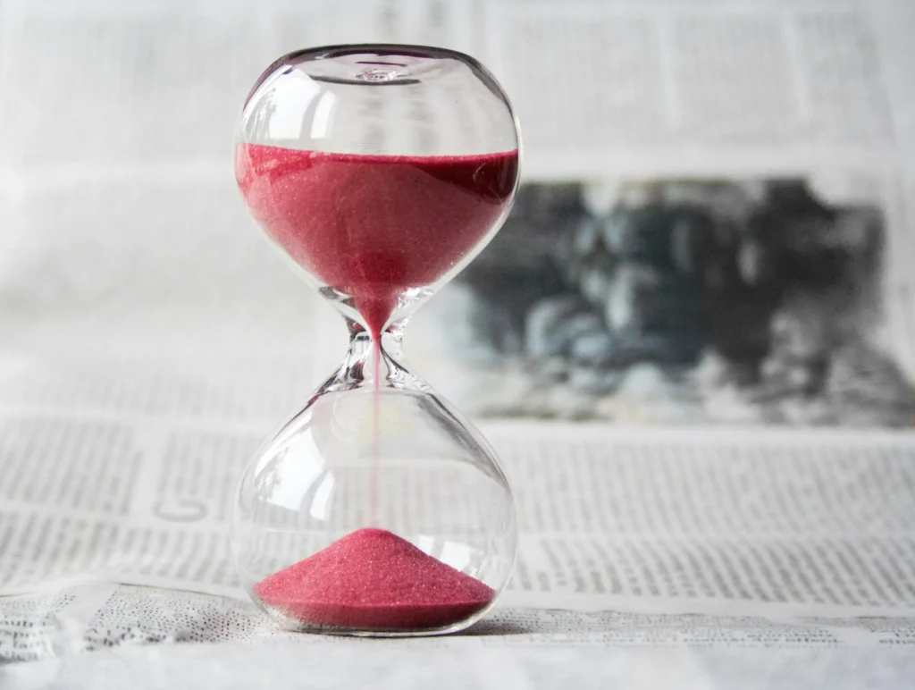 Close-up of a transparent hourglass with pink sand flowing, placed on a newspaper background showing how time flows quickly for teachers in the classroom