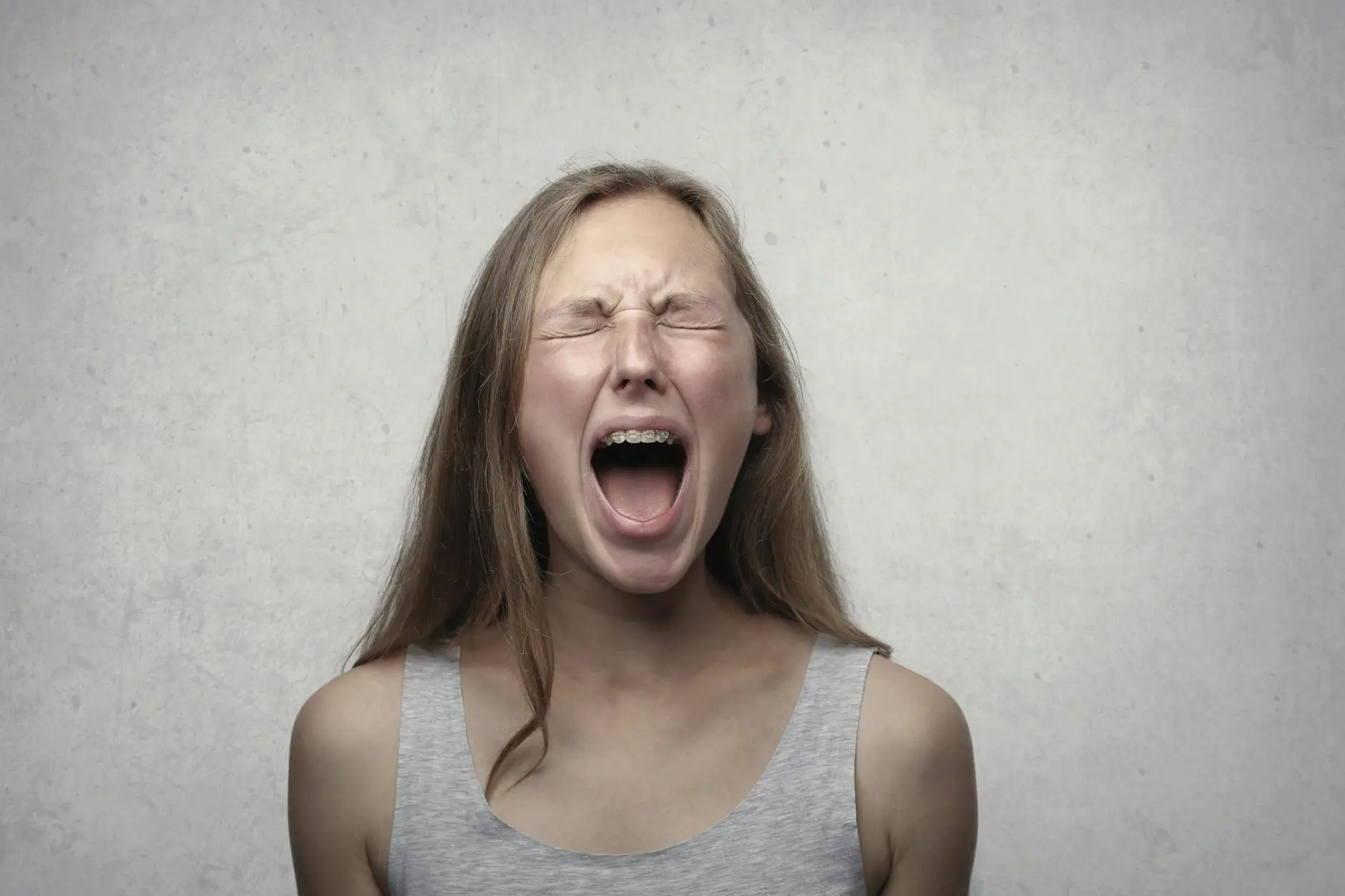 A teenager in gray tank top squeezes her eyes shut and screams at the top of her lungs.