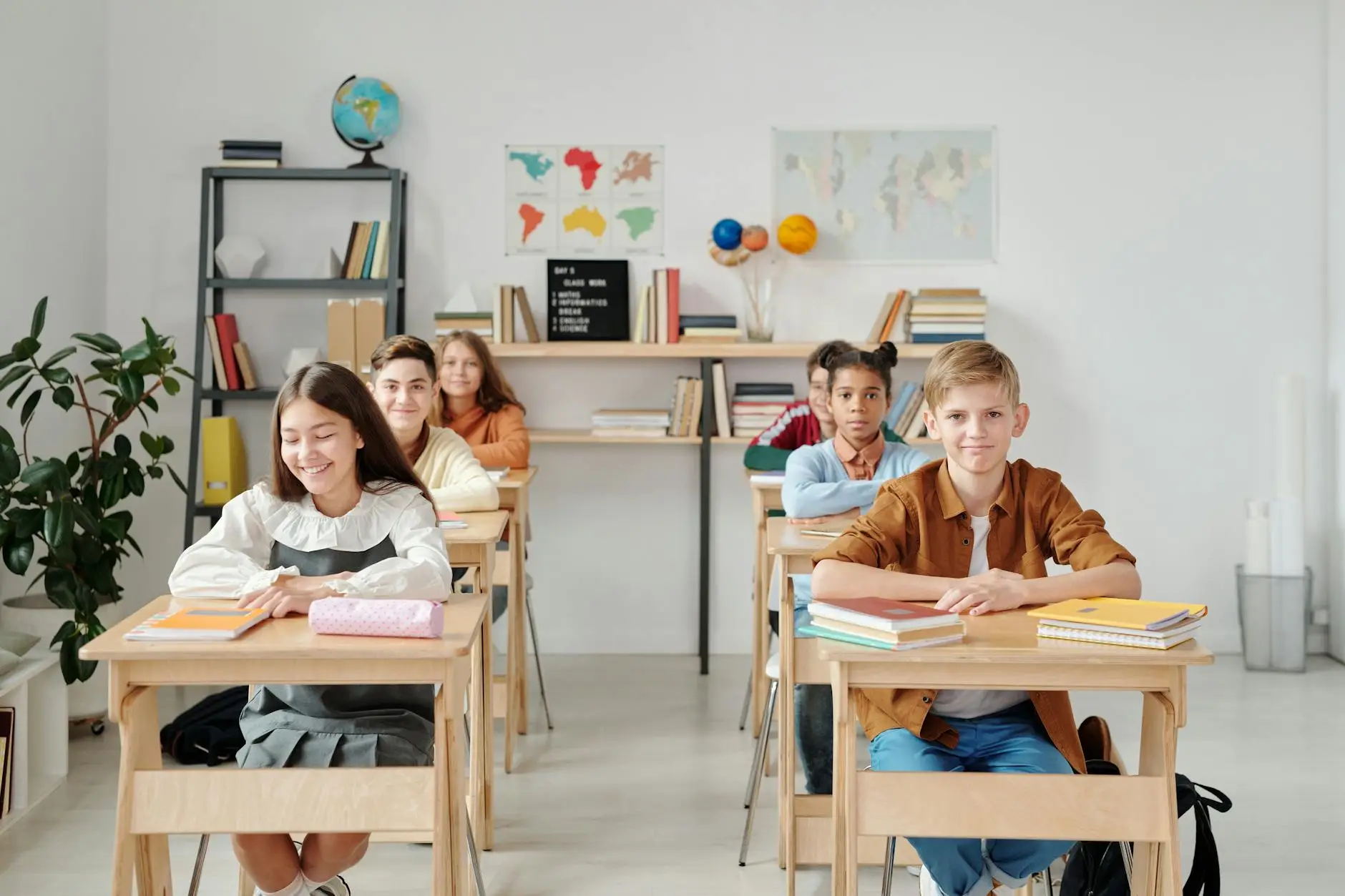 Students sit in orderly rows, feet below their desks, hands folded, showing the order that comes with building and implementing a strong classroom management plan