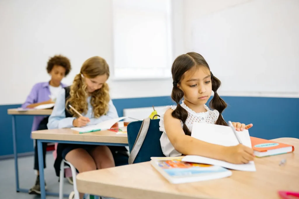 Three students sit at their desks and write on papers.