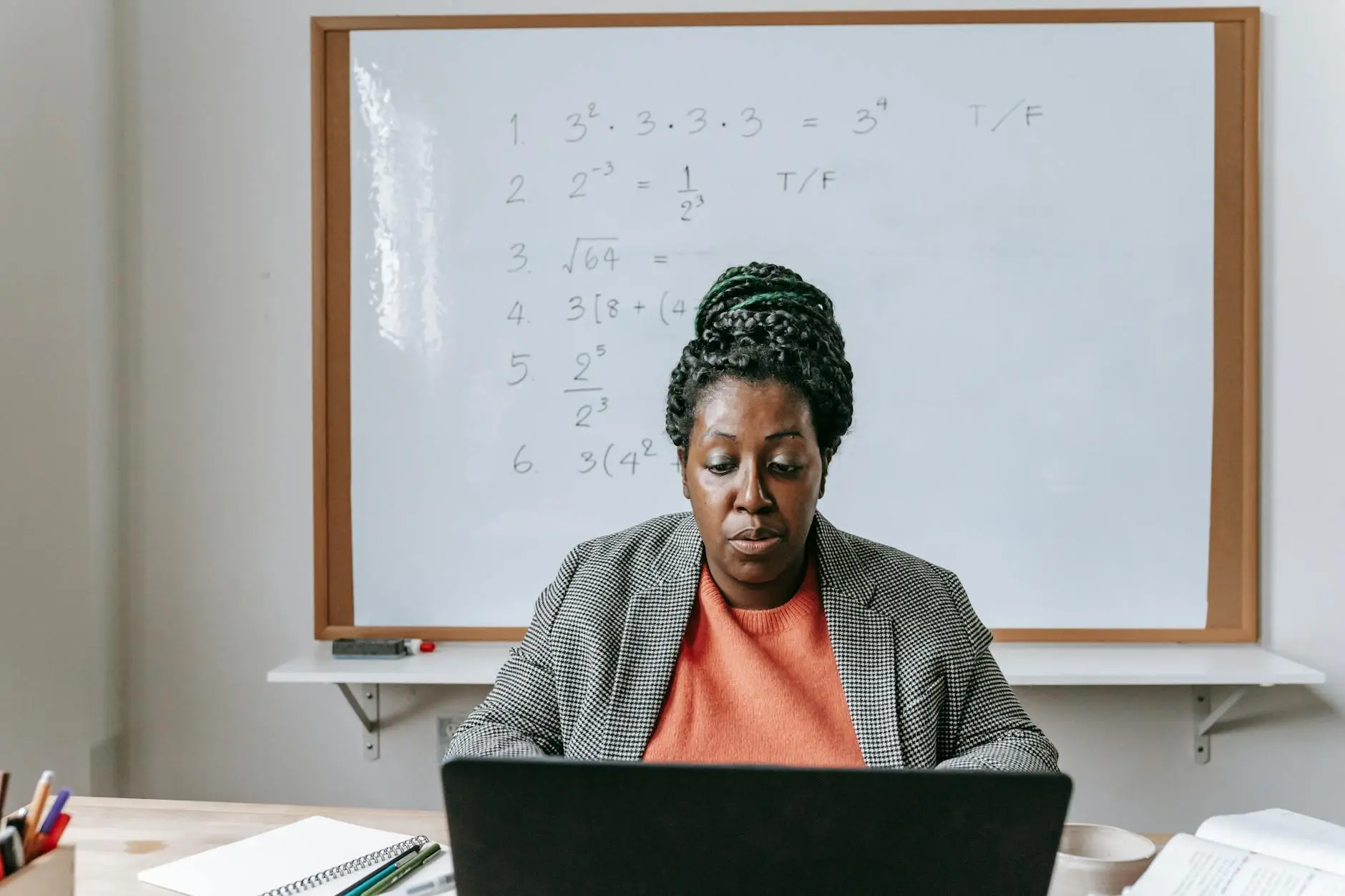 A teacher sits at her desk in front of a computer, taking notes to remember details and action items after parent-teacher conferences