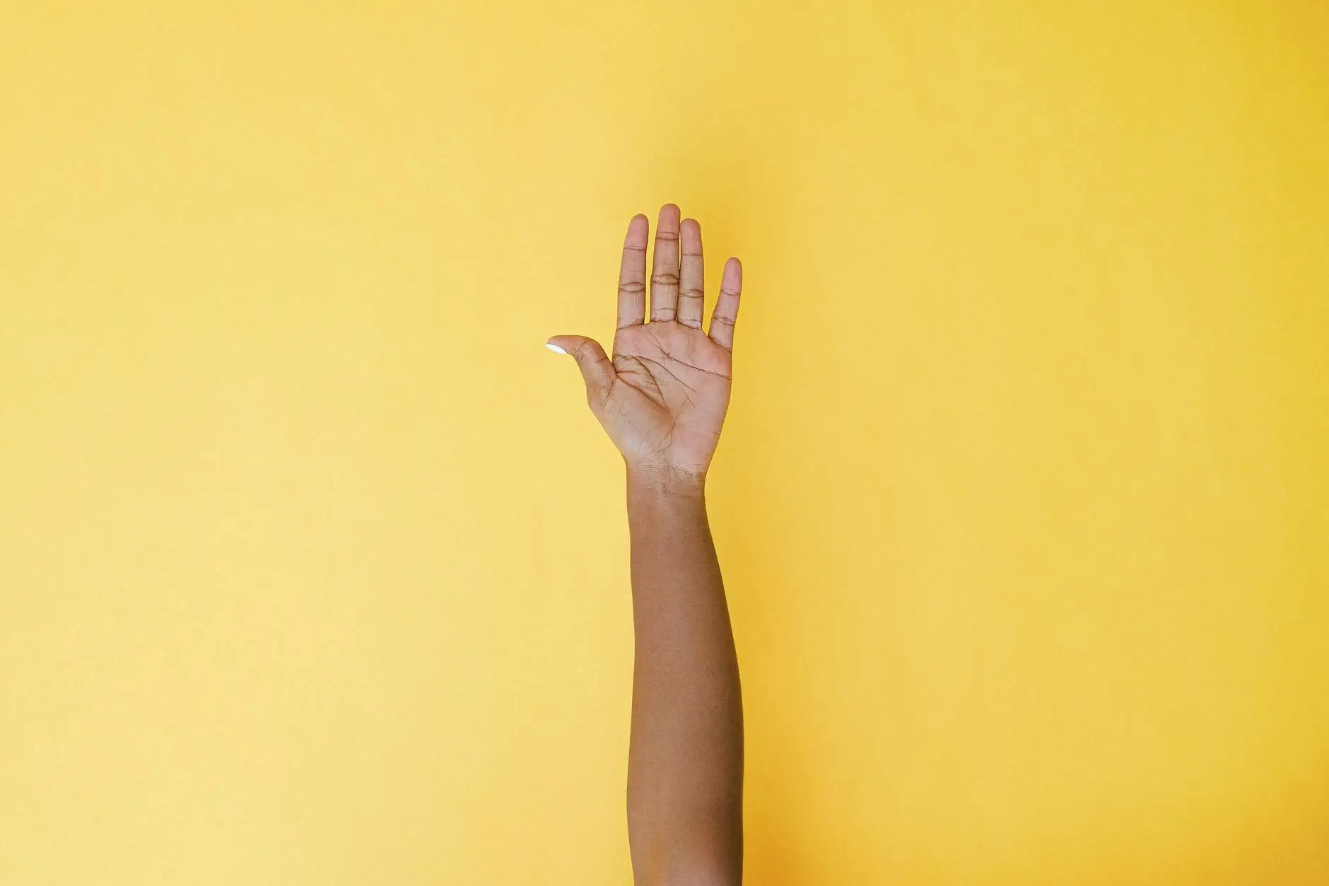 A hand is raised against a yellow background, showing an effective quiet signal to use in noisy classrooms