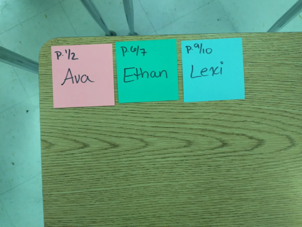 Three sticky notes with names in the upper left corner of a student desk, showing how to label middle school student desks with student names