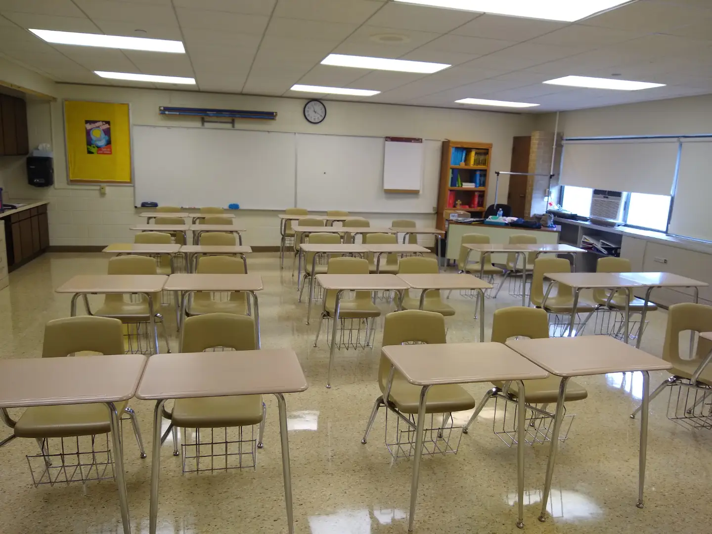 A bright classroom with desks in pairs and rows stretching toward the back of the room