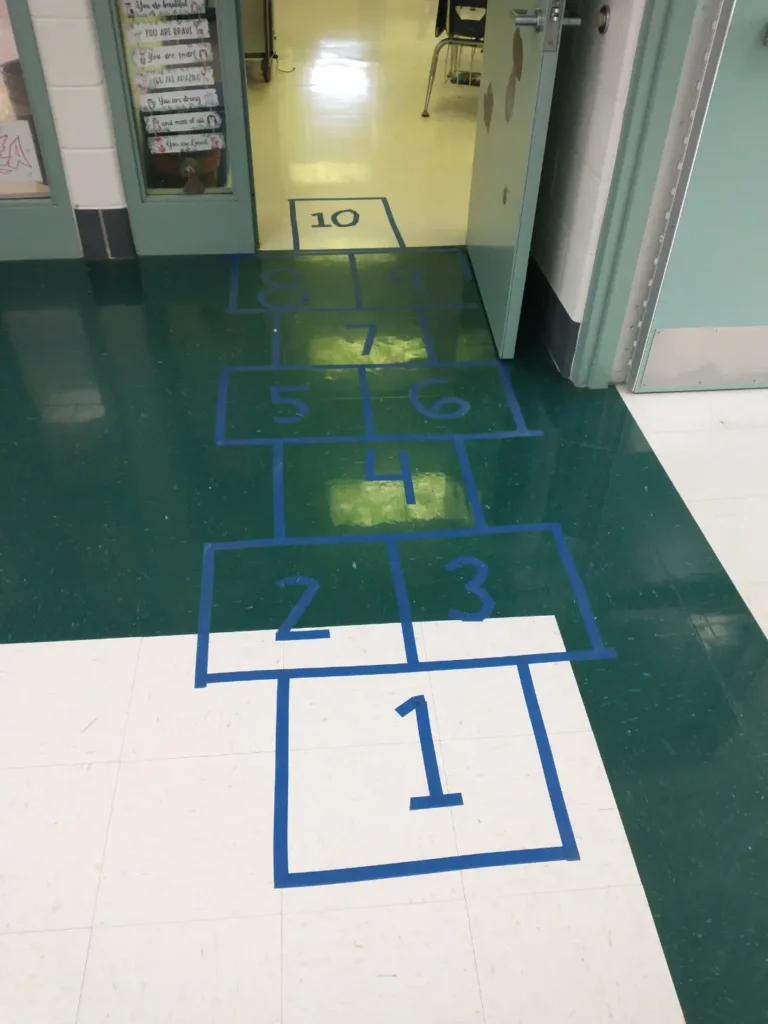 A photograph of a hopscotch game outside of a school classroom made with blue tape on the tile floor