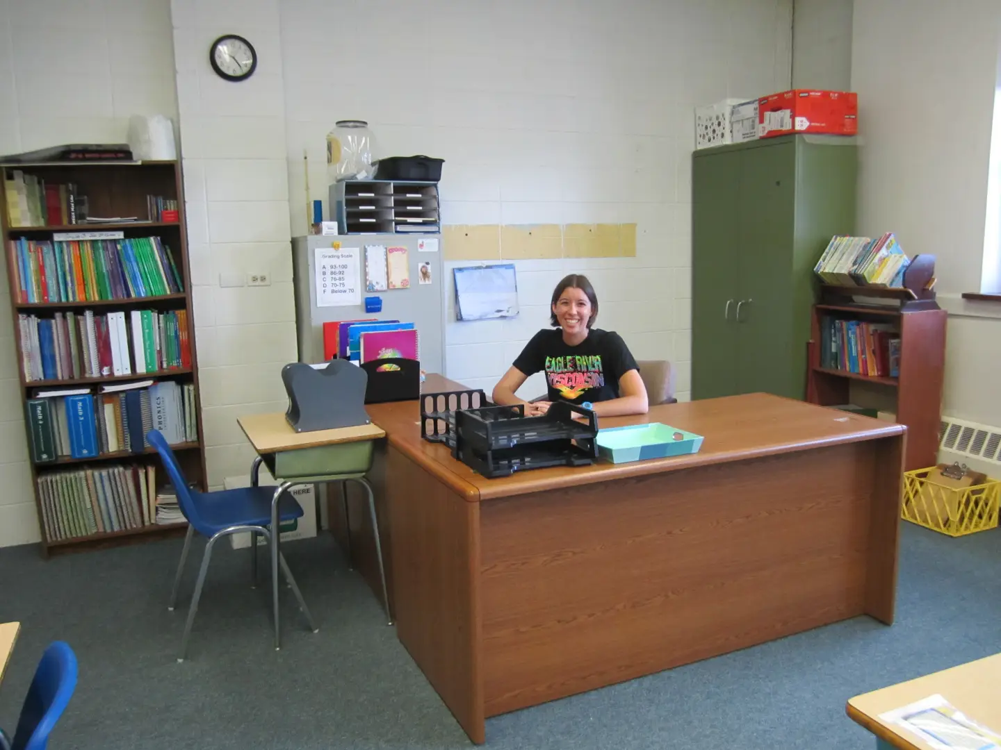 Tori sits at her organized teacher's desk, grinning proudly and ready for back to school season