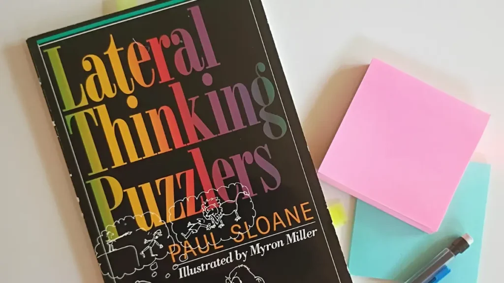 The cover of the book Lateral Thinking Puzzlers by Paul Sloane with sticky note pads and a pencil in the corner